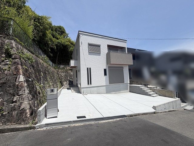 高槻市大和1丁目　新築一戸建 爽やかな青空が広がる現地写真。白を基調としたシンプルな外観デザインが、自然豊かな周辺環境に調和しています。広い駐車スペースも魅力です。